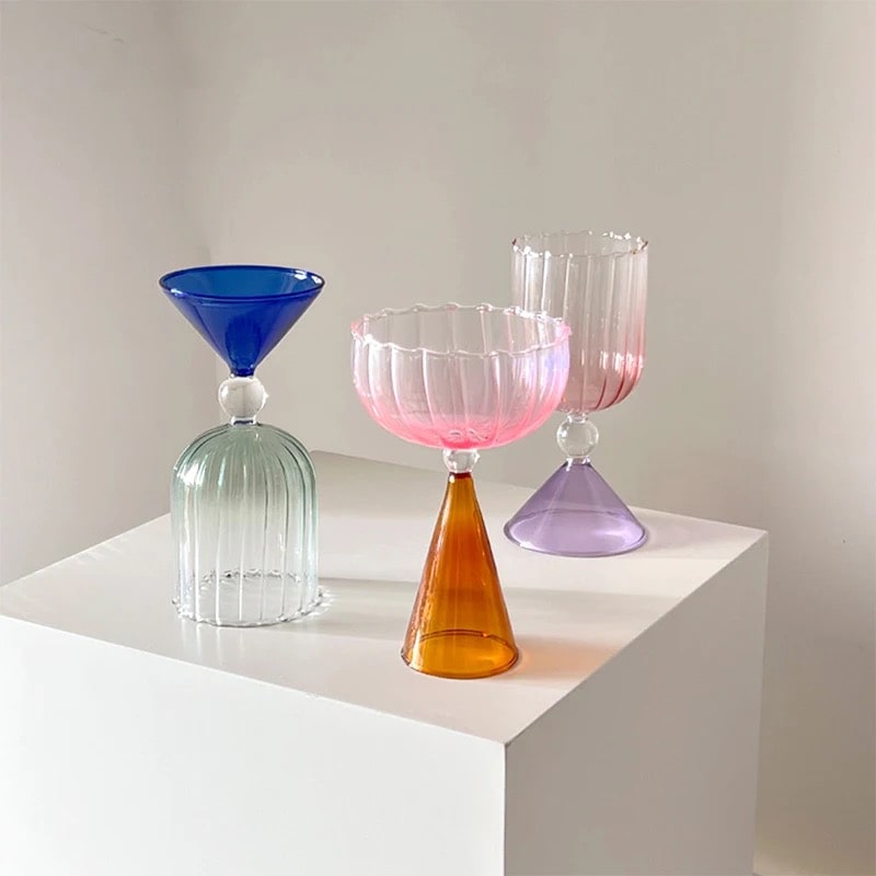 Colorful cocktail glass with gold rim, pink stem, and clear bowl displayed against neutral background.
