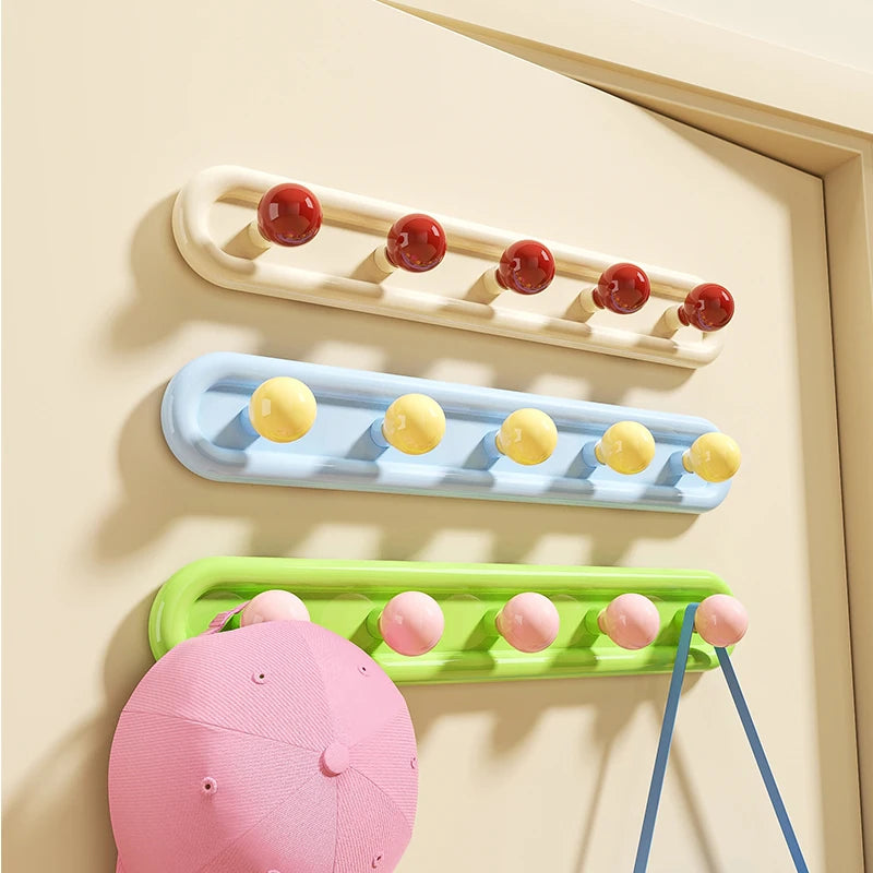 Colorful decorative wall hooks mounted on beige wall with pink cap and blue handbag hanging.