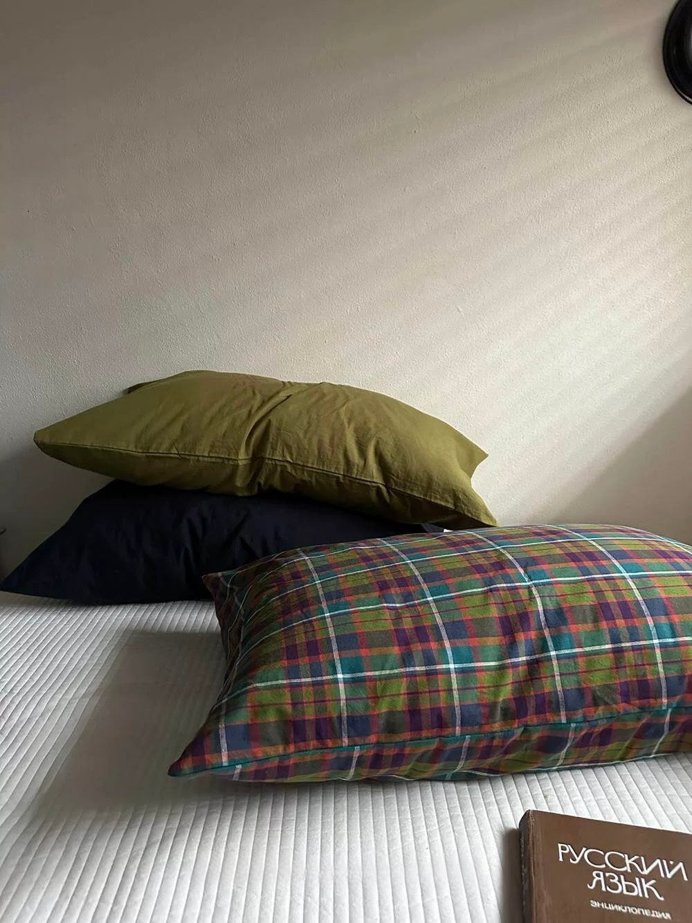A colorful plaid pillowcase in front of olive green and navy pillowcases on white bedding.