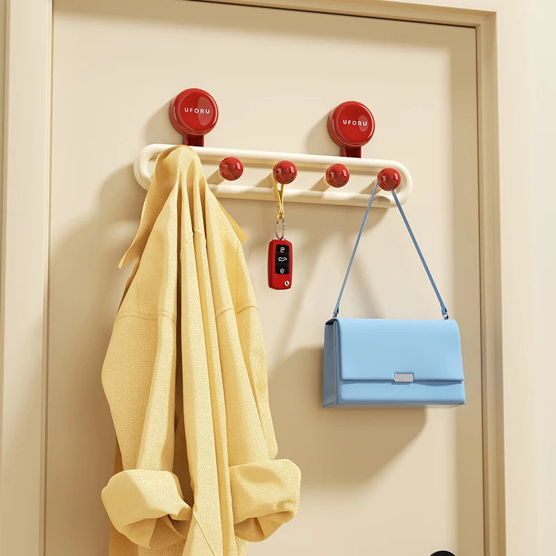 Wall-mounted hook rack with red hooks holding a yellow jacket, blue handbag, and red keychain on a beige wall.