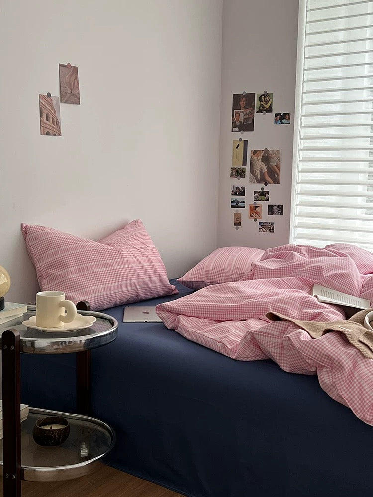 Bedroom with pink checkered bedding and pillows, nightstands with cups and books.
