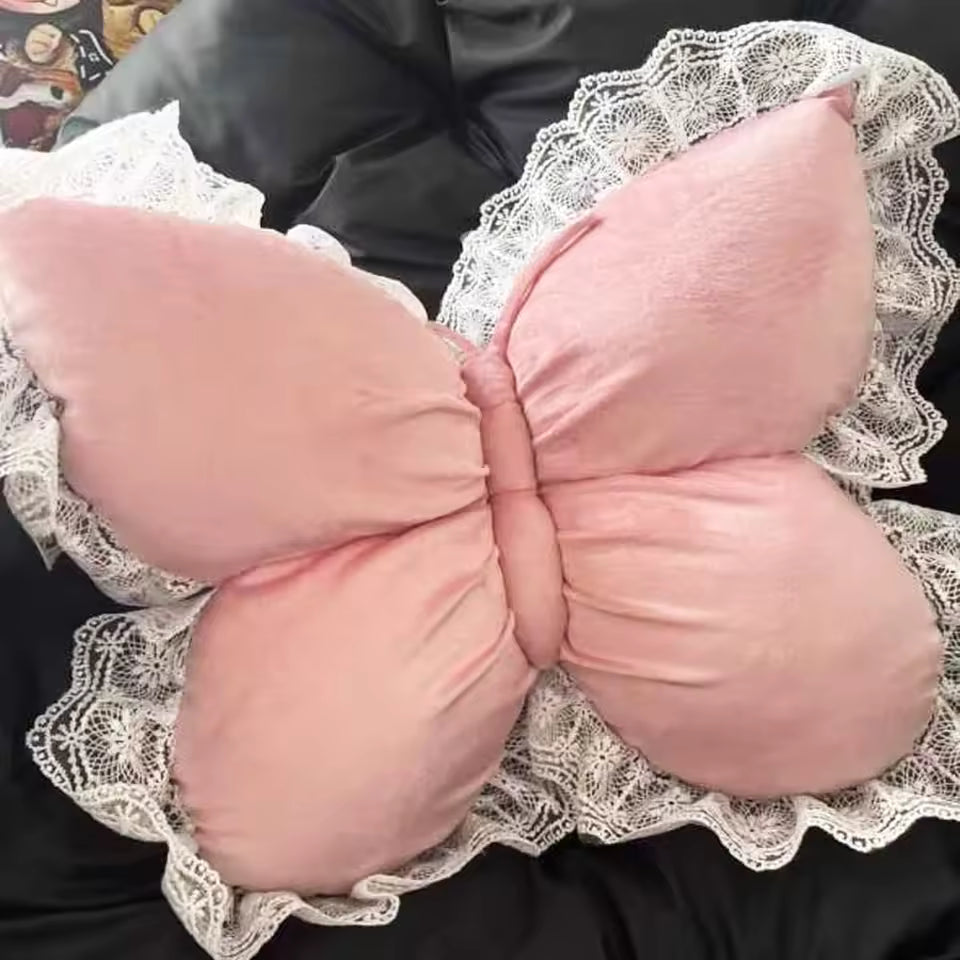 Pink butterfly-shaped cushion with lace trim on a dark background