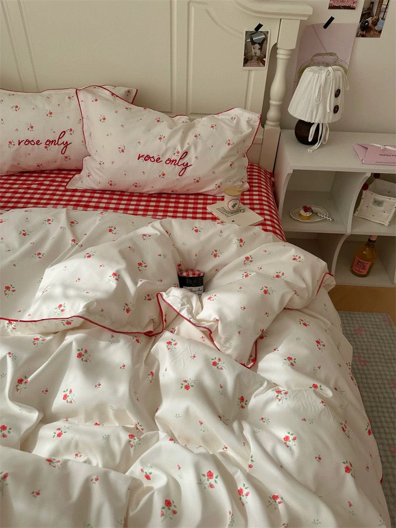 Bedding set with floral pattern and 'rose only' text on a bed with red checkered blanket.