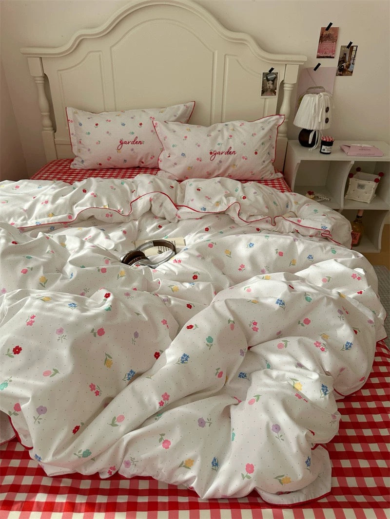 White floral comforter on a bed with red checkered sheets in a bedroom setting.