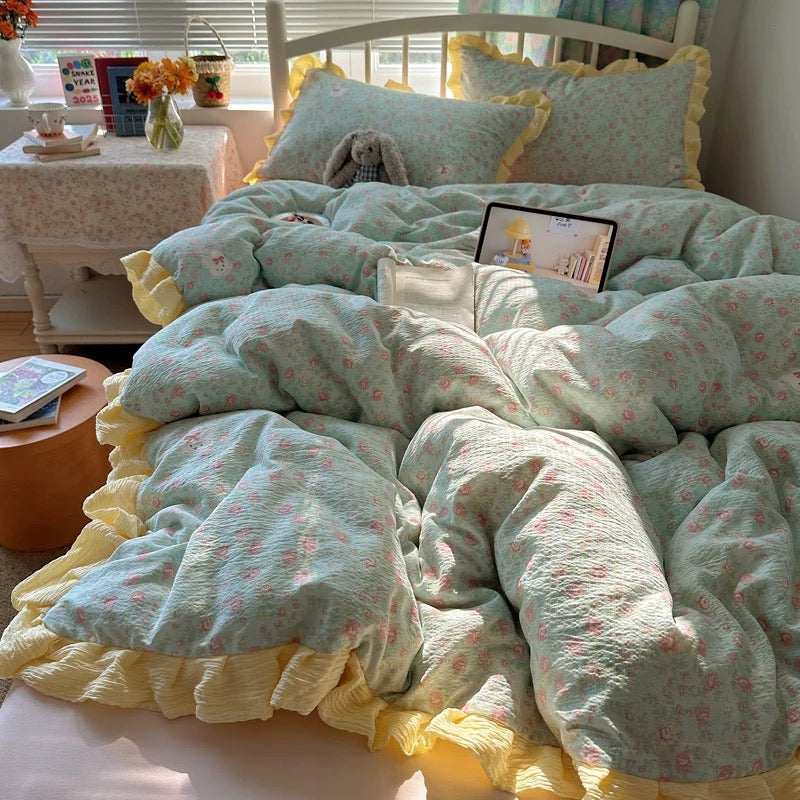 Two floral ruffle pillowcases arranged on a bed beside an open book and plush bunny
