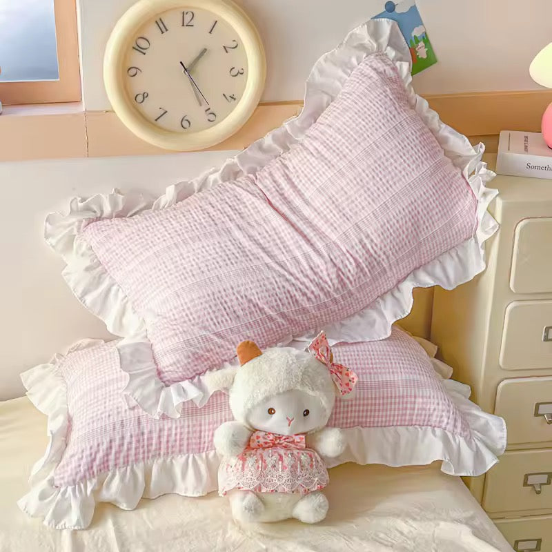 Pink ruffled pillows with a white teddy bear on a bed in a bedroom setting.