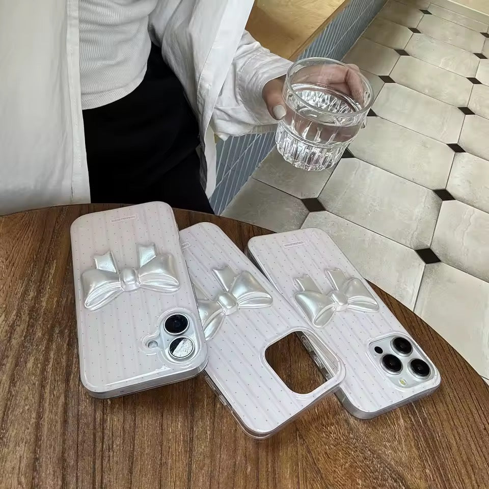 Three phone cases with bow designs on a wooden table, with a person holding a glass in the background.