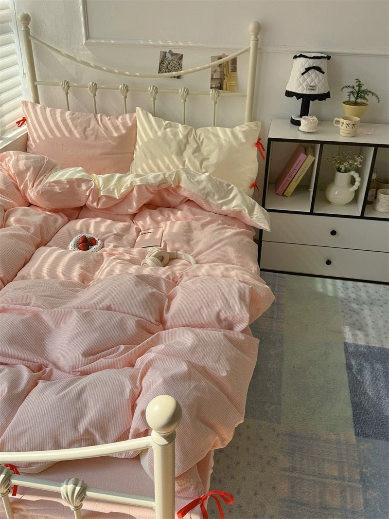 Pink and white bedding set on a bed with a nightstand in the background.