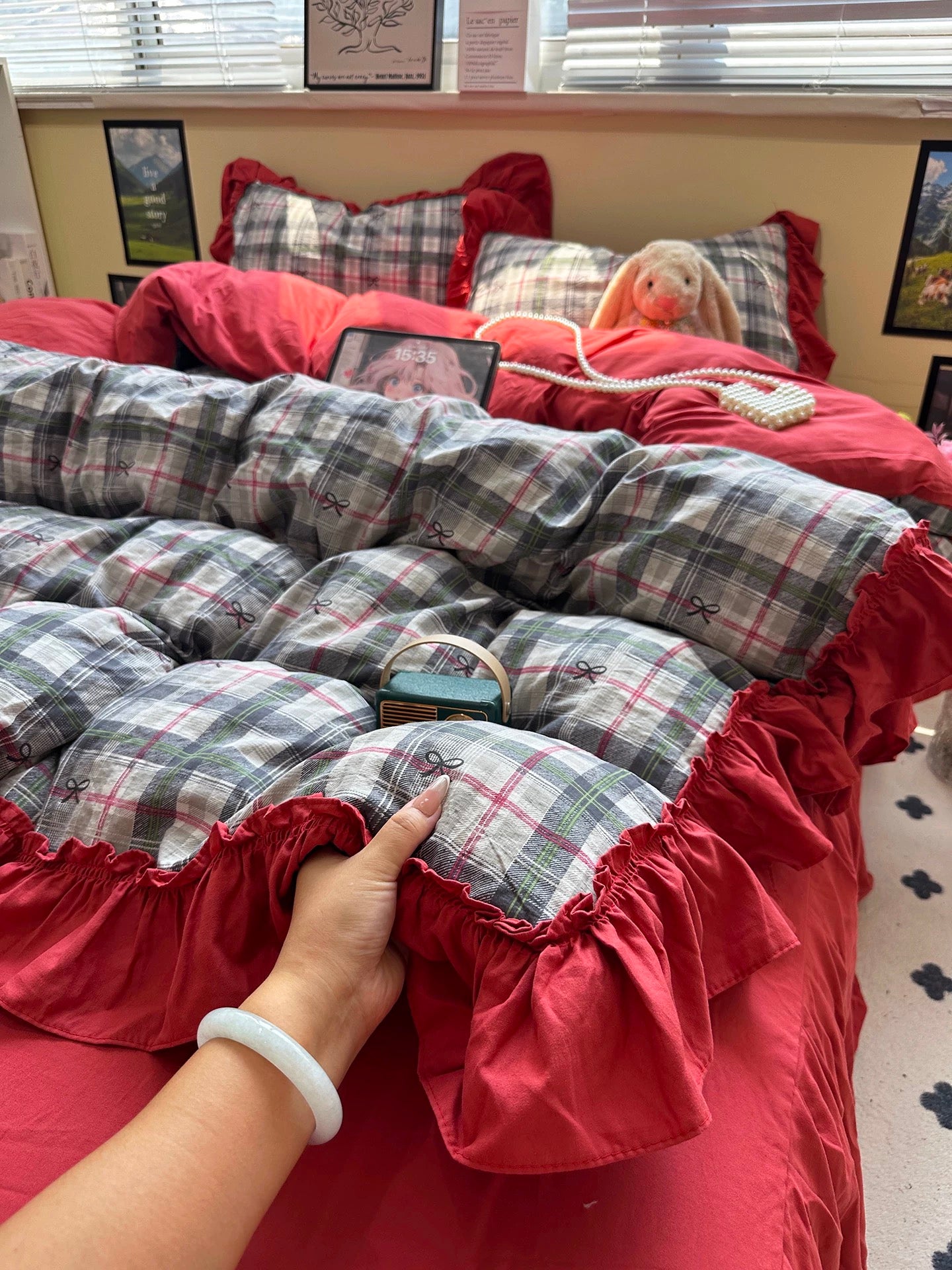Person adjusting red and plaid bedding on a bed with a window in the background.
