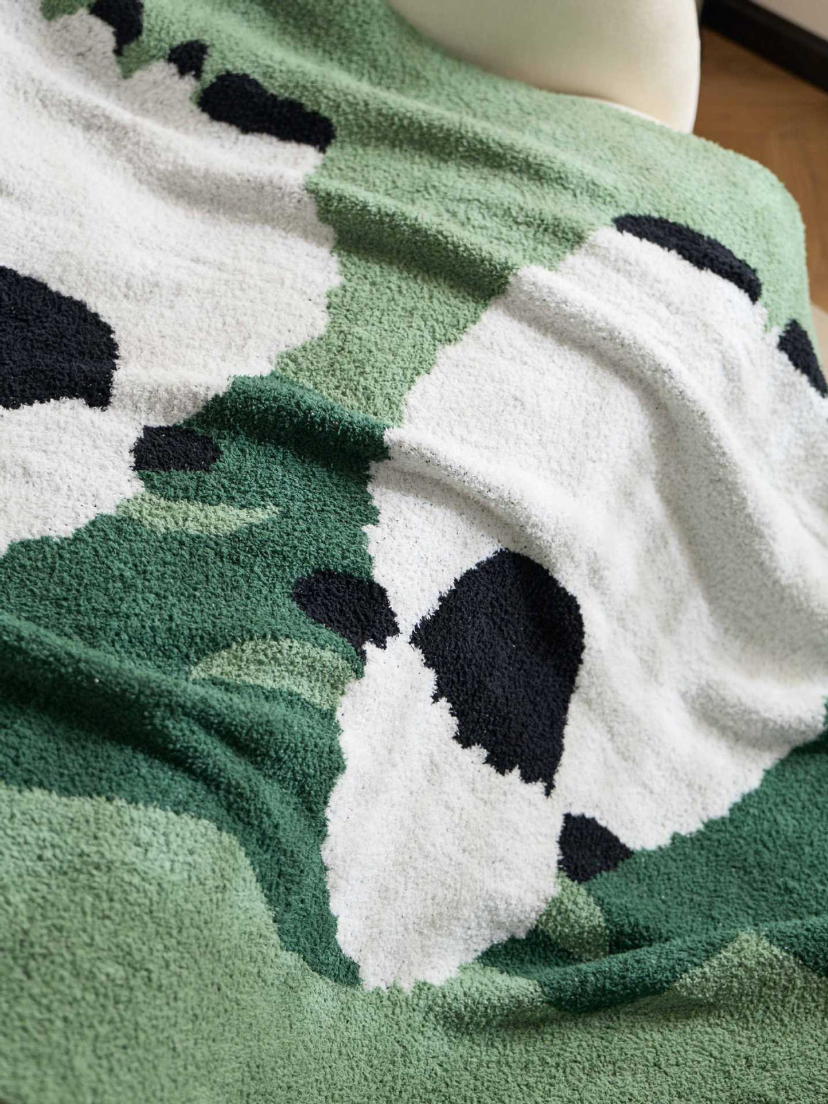 A close-up of a plush towel draped over a mannequin, featuring a green and white camouflage pattern with black spots.