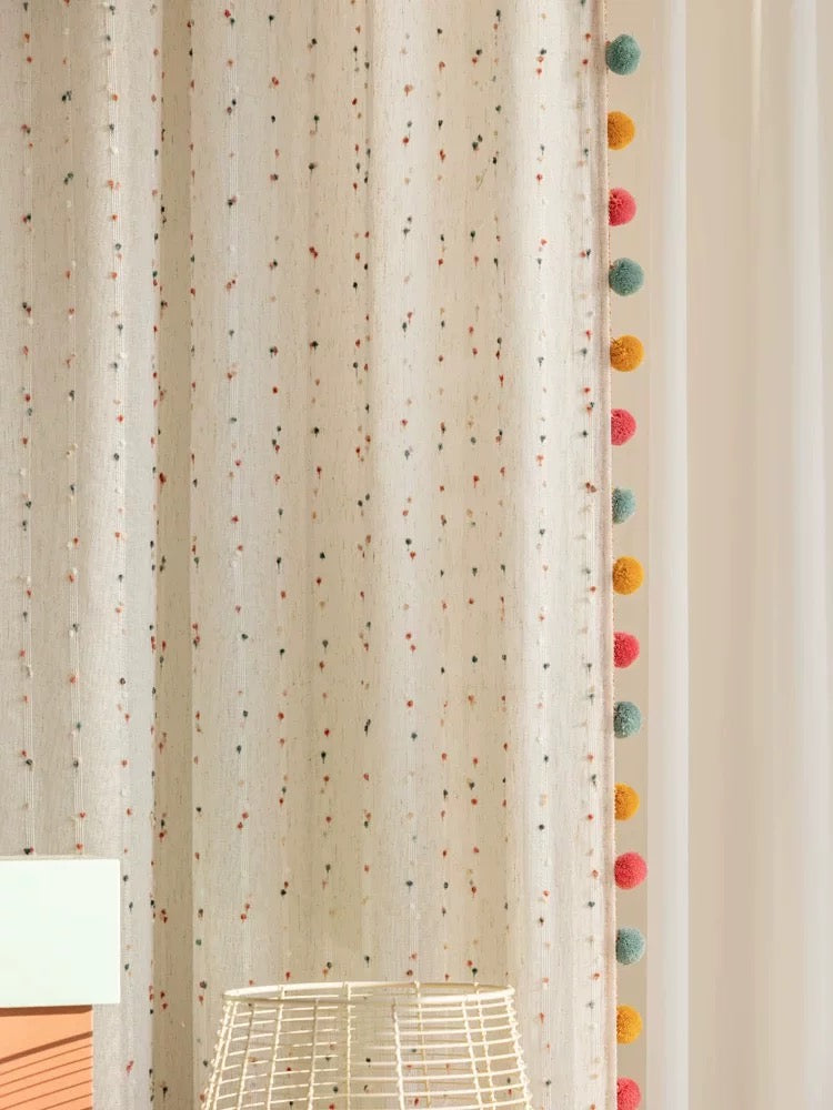 Close view of cotton-linen curtain with tiny rainbow embroidery and colorful pom-pom edge