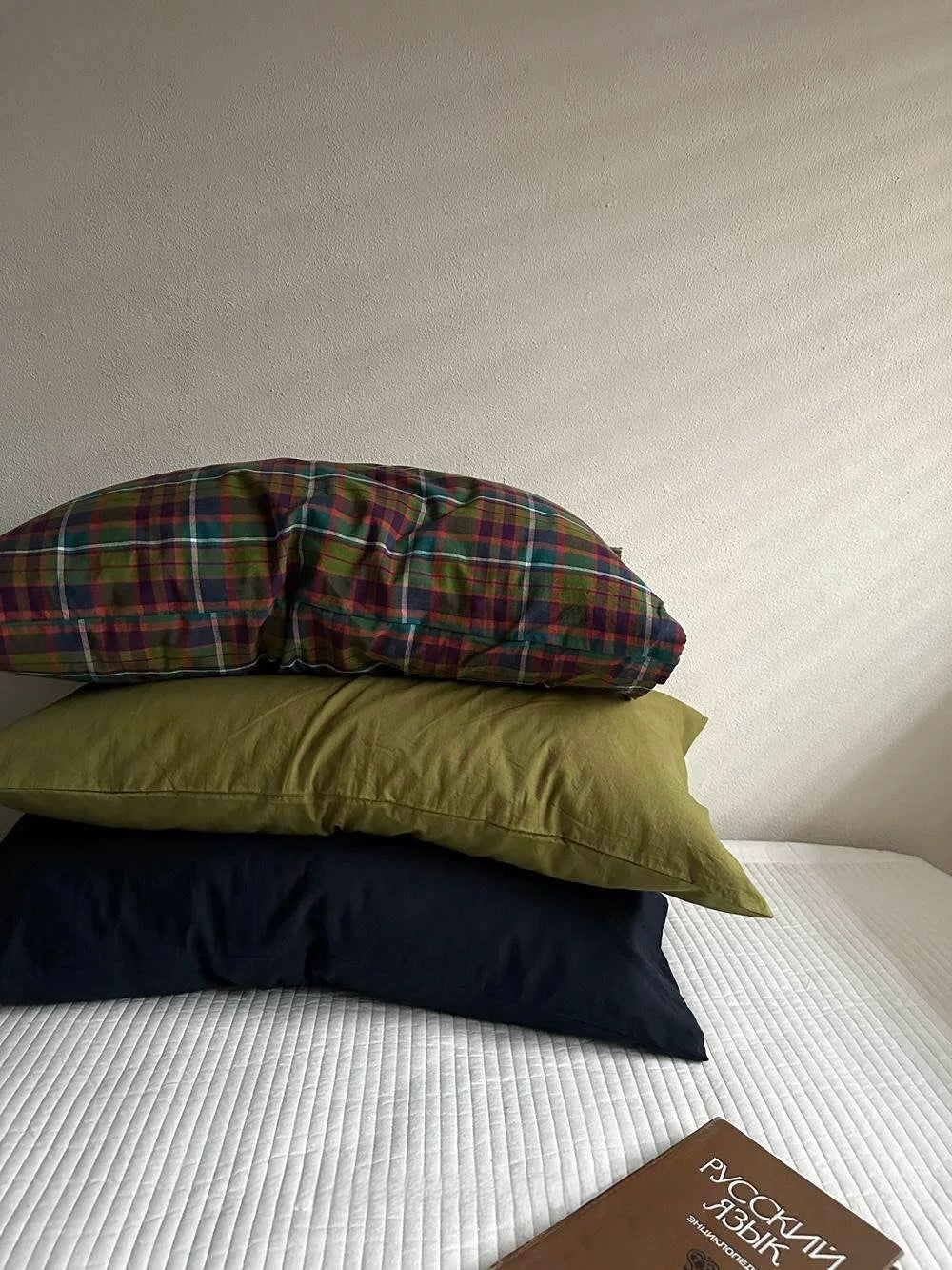 A washed cotton pillowcase set stacked with plaid on top, olive green in the middle and navy below.