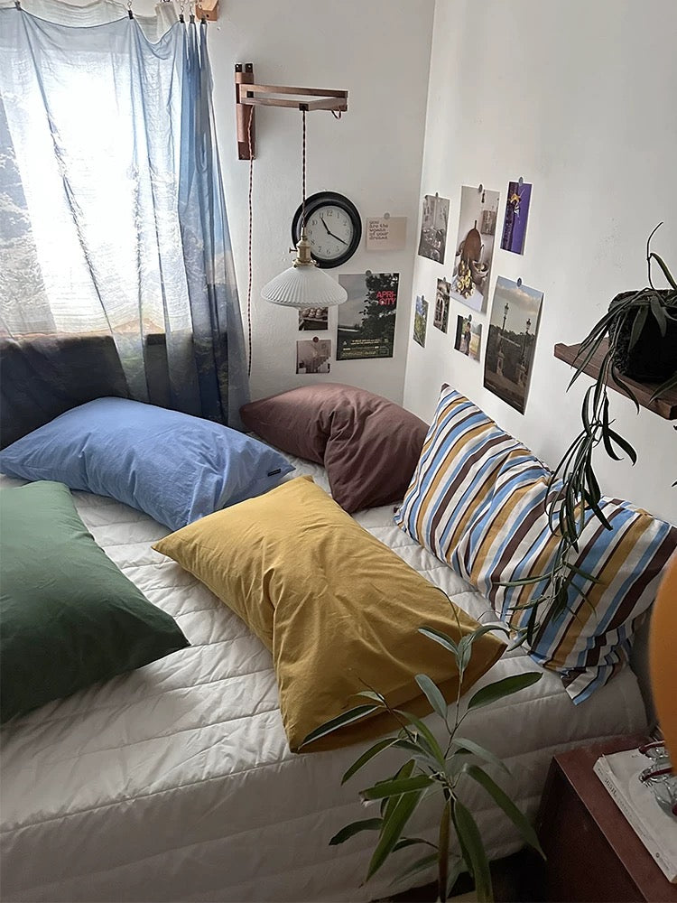 A side view shows solid blue, mustard and green cotton pillowcases with mocha and striped designs behind them.