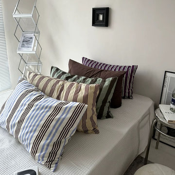 Bed with striped pillows and a small shelf in a room.