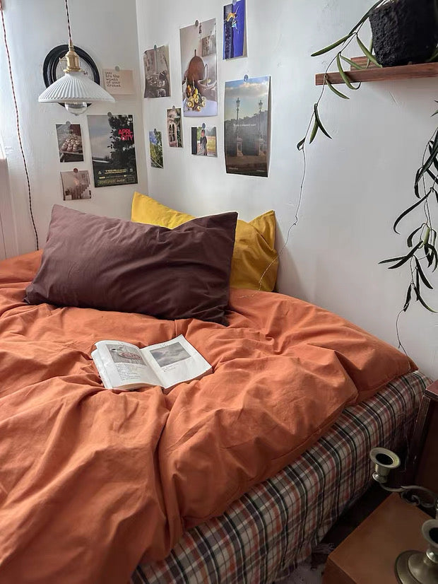 Bedroom with orange bedding, pillows, and a book open on the bed.