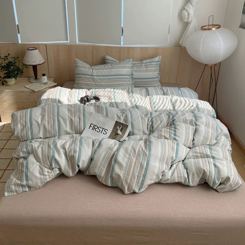 Striped bedding set on a bed with pillows and a 'FIRSTS' card.