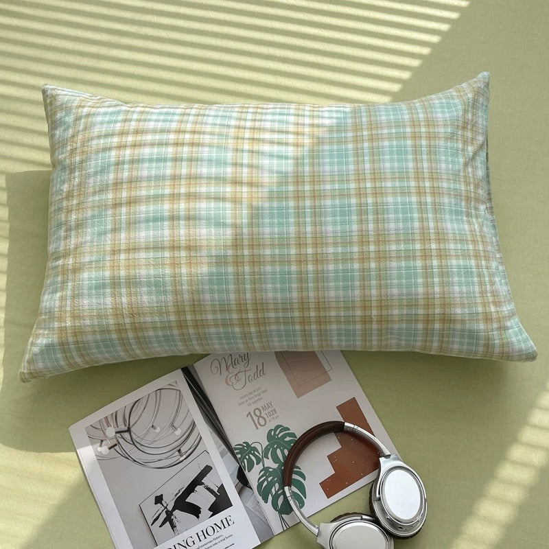 Plaid pillow on a light green surface with a magazine and headphones.