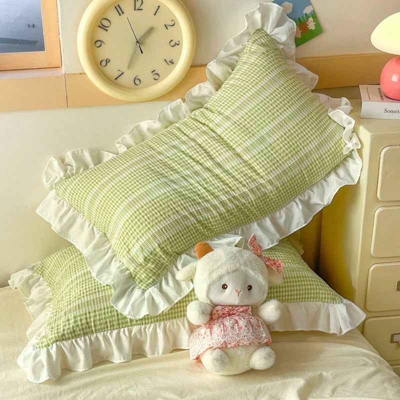 Green checkered pillows with white ruffles and a plush toy on a bed.