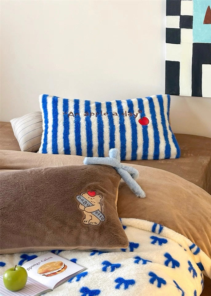 Striped pillow with text and red apple on a couch with brown pillow and blanket