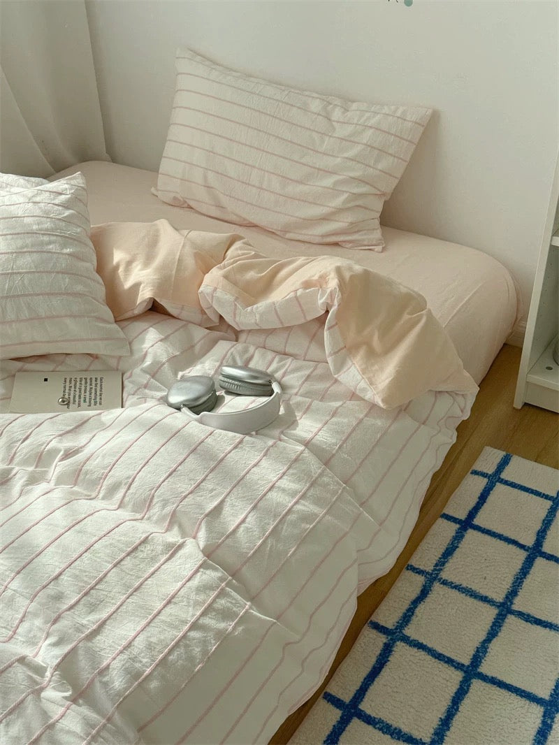 Neatly made bed with striped bedding and pillows in a room with a blue grid rug.