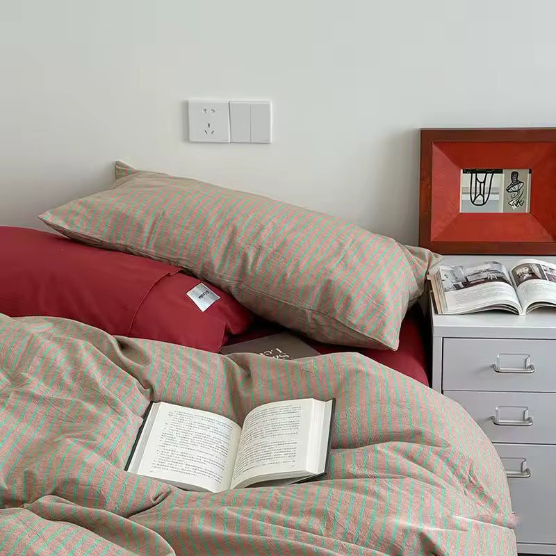 Bed with striped bedding and pillows, open book, and a nightstand with an open book.