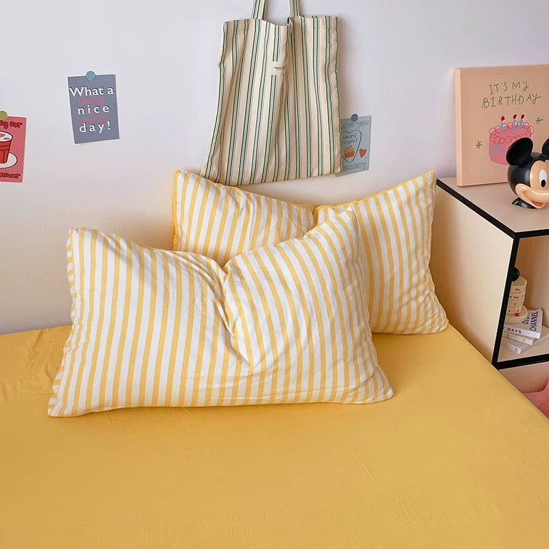 Yellow and white striped pillows on a bed with a striped bag and decorative items in the background.