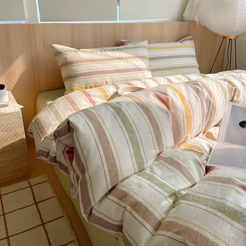 Striped bedding on a bed in a room with a lamp and window.
