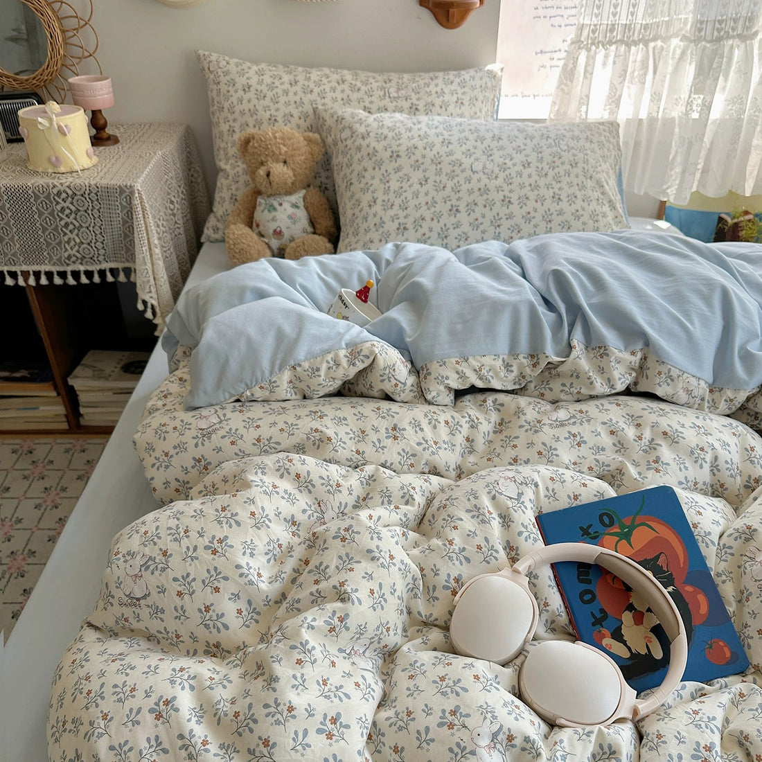 Floral patterned comforter on a bed in a bedroom with a teddy bear and decorative items.