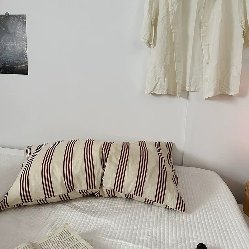 Striped pillow on a bed with a white wall and hanging fabric in the background