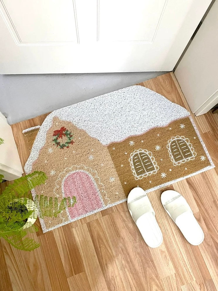 Cream gingerbread house entryway mat styled beside a plant and white slippers