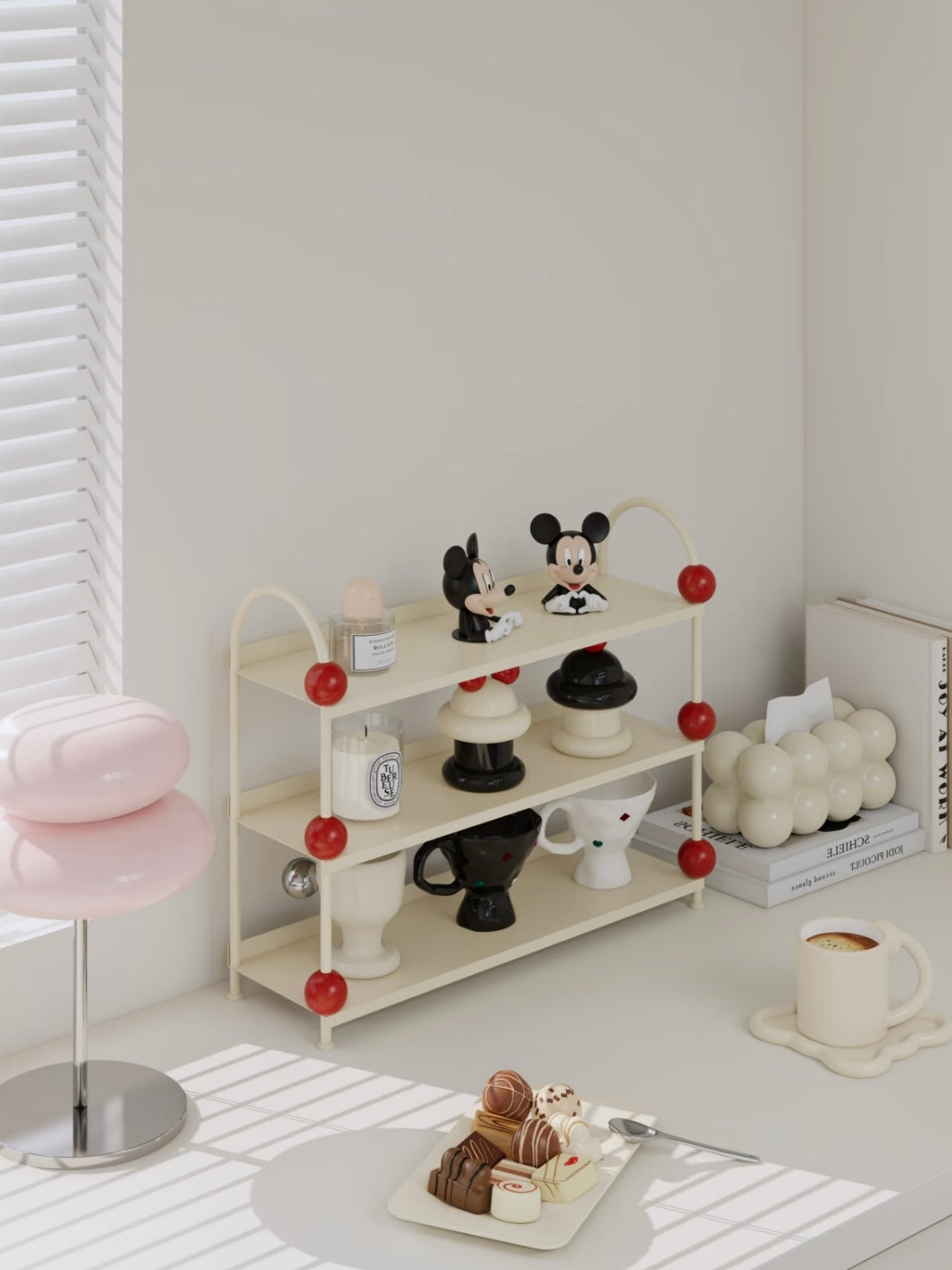 Cream tabletop shelf viewed at an angle with red ball accents and small objects on its three open tiers.