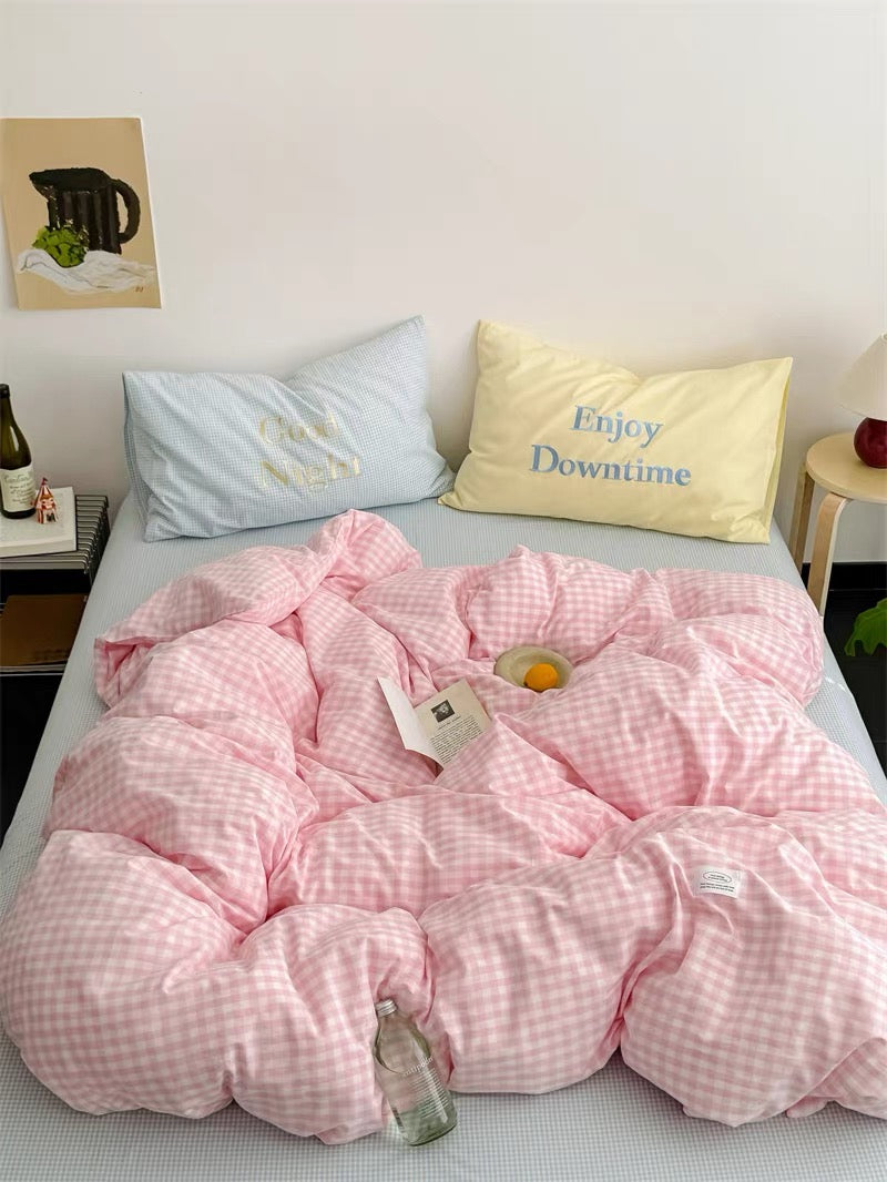 Pink checkered comforter on a bed with pillows and a bottle of wine.