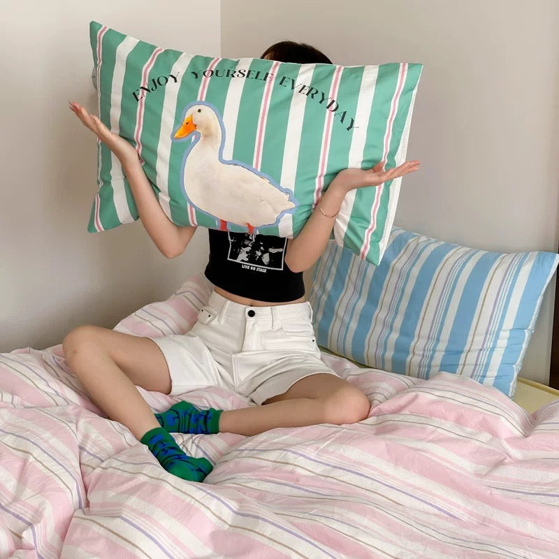 Person sitting on a bed with a decorative pillow featuring a duck and text.