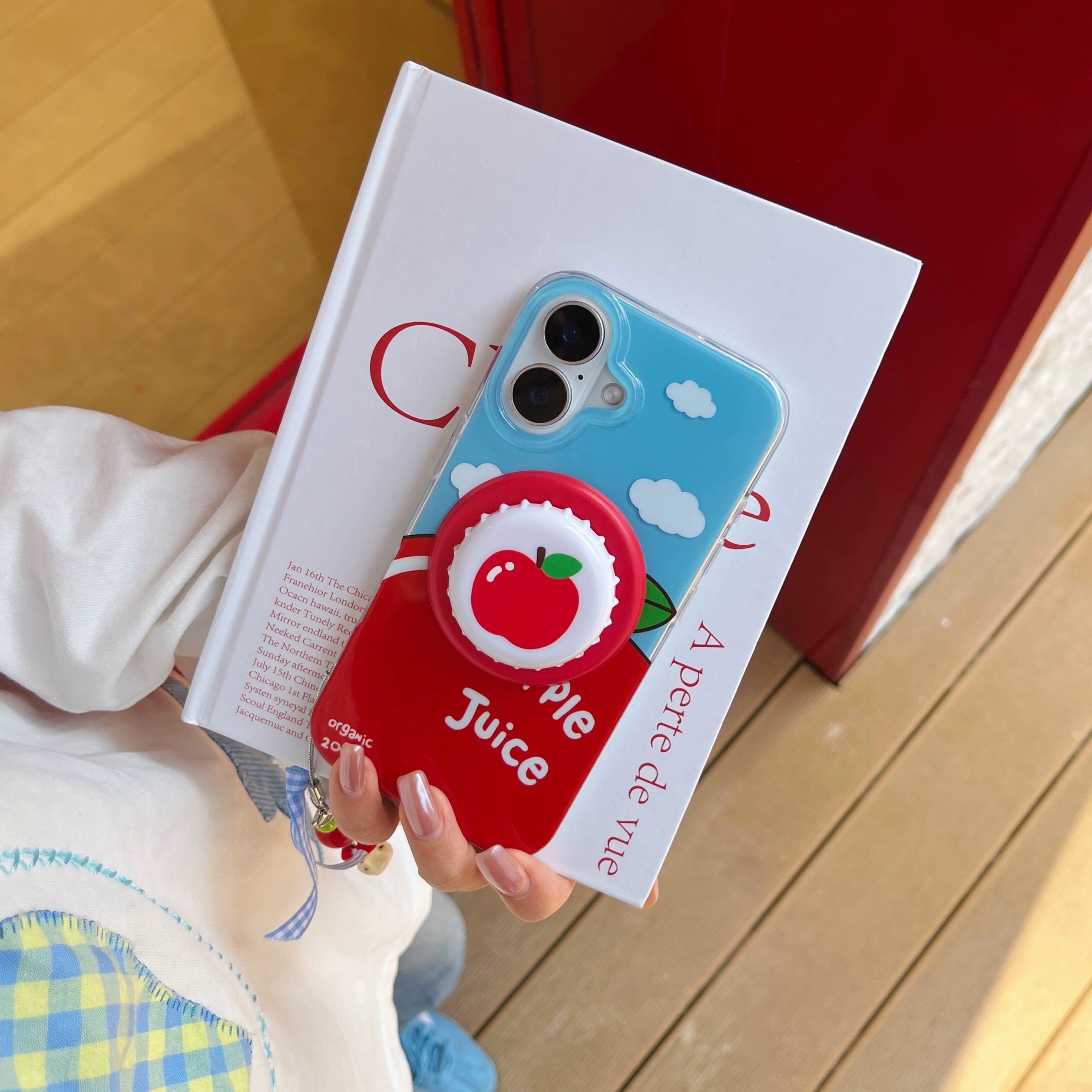 Phone case with apple design held over an open book on a wooden surface