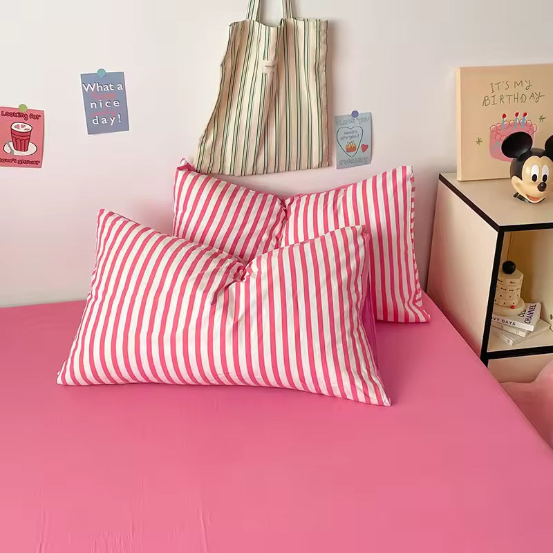 Pink bed with red and white striped pillows, next to a shelf with decorative items.