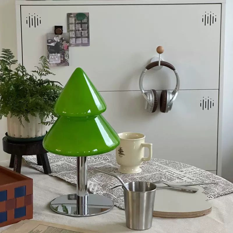 Green stool with a metallic base on a table with a cup and plant in the background.