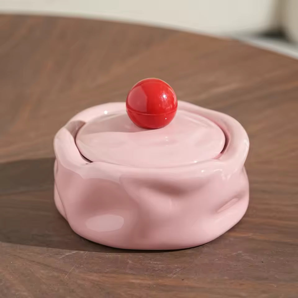 Pink ceramic container with a red ball on top on a wooden surface