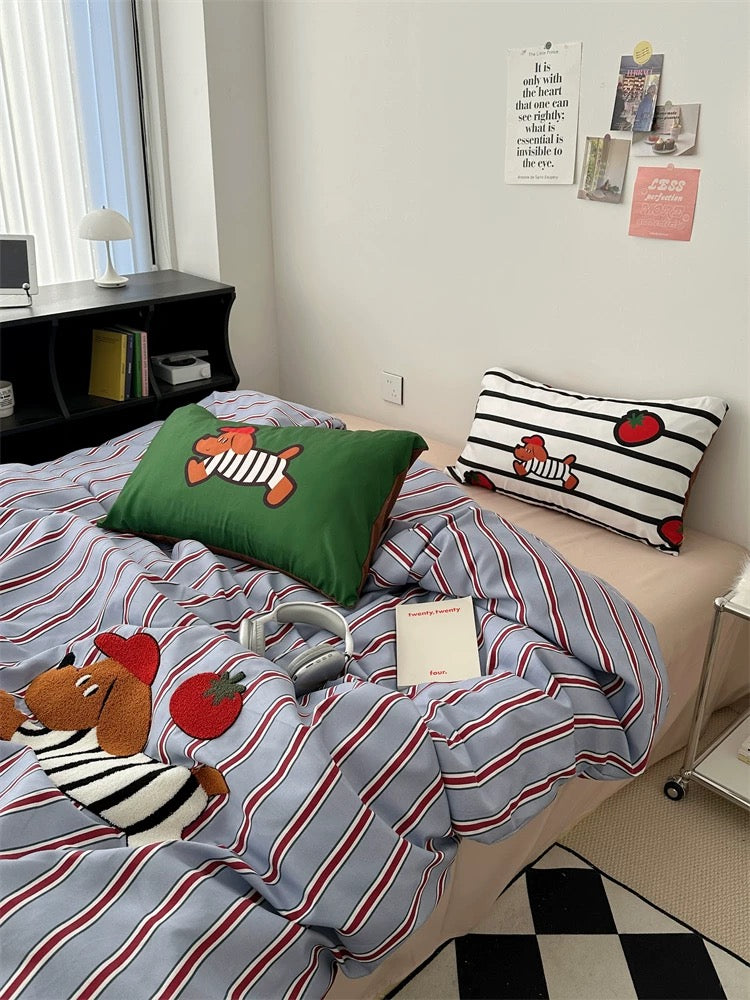 Bed with striped bedding and cartoon-themed pillows in a room with a desk and window.