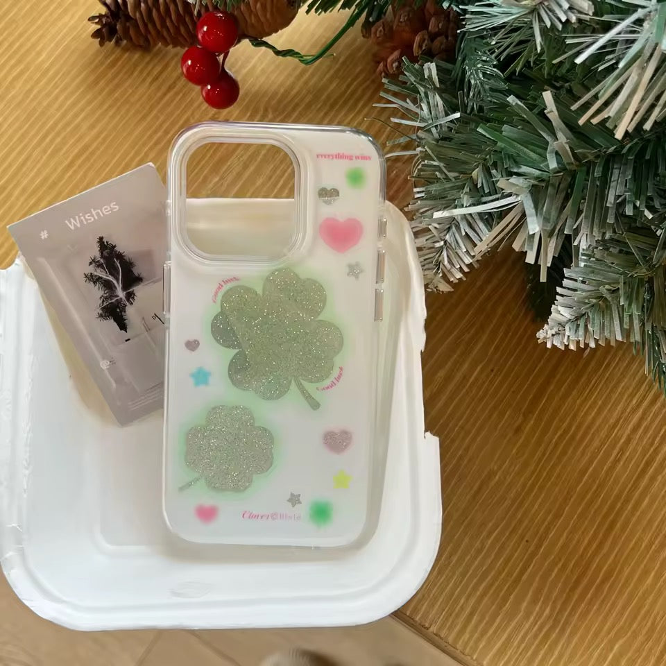 Phone case with clover design on a wooden surface with Christmas decorations.