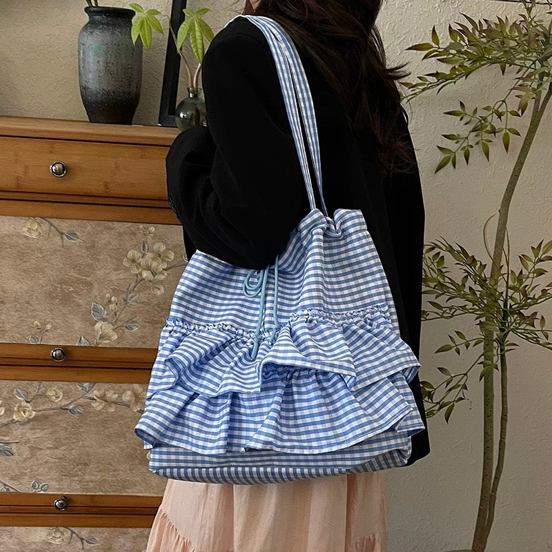 Person wearing a blue and white checkered drawstring bag with ruffles, standing in a room with floral wallpaper.