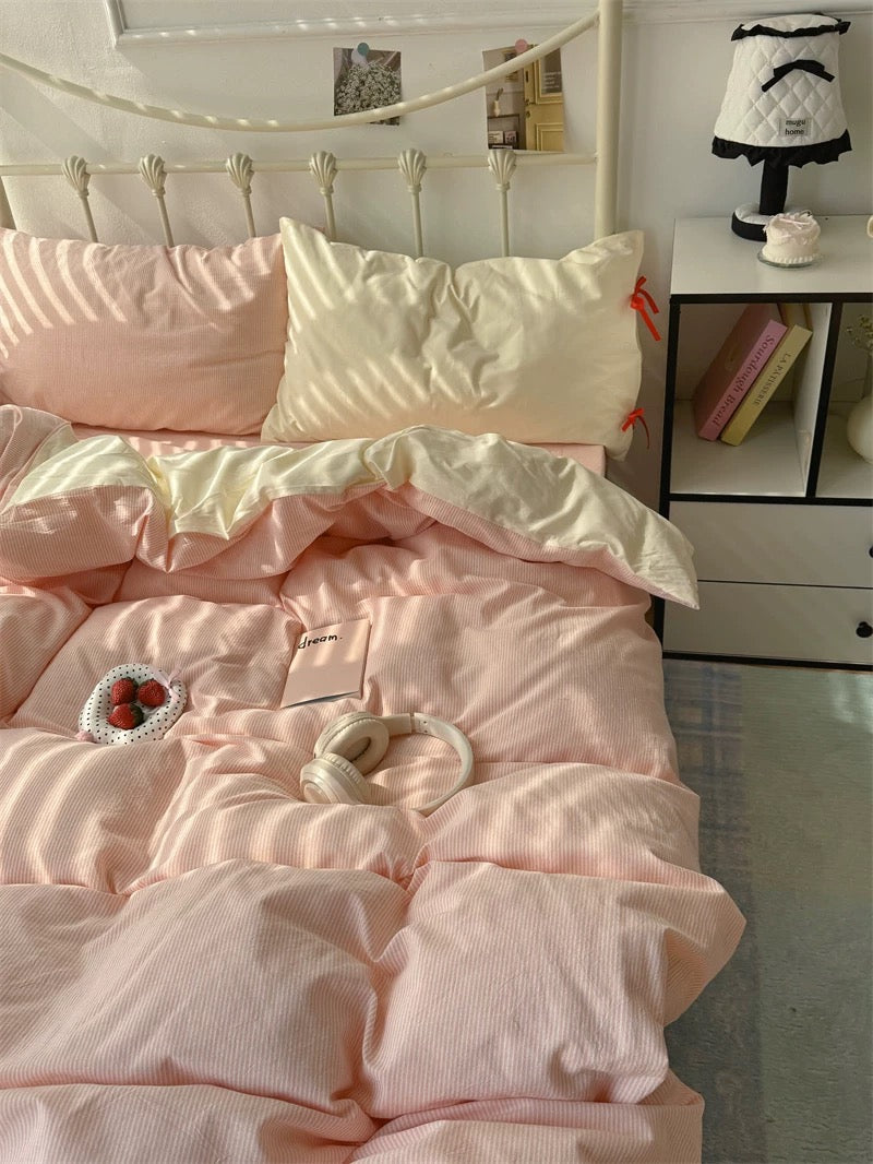 Pink comforter on a bed in a room with a nightstand and decor items.