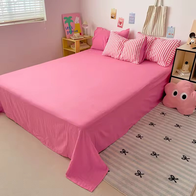 Bedroom with pink bedspread and striped pillows, featuring a small nightstand and decor items.