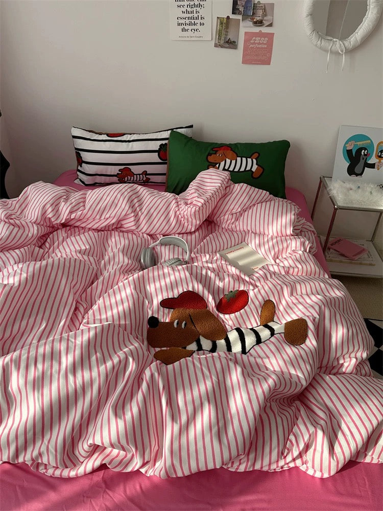 Bed with pink and white striped bedding, colorful pillows, and a teddy bear on a bed in a room.