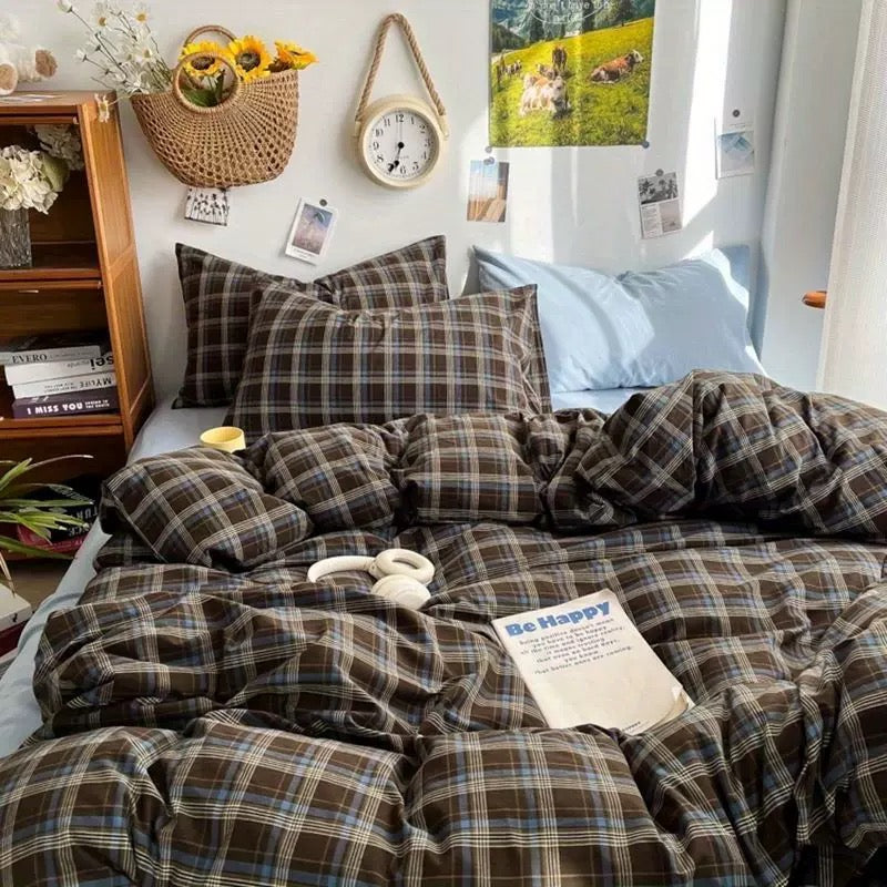 Plaid bedding set on a bed with pillows and a book in a bedroom setting.