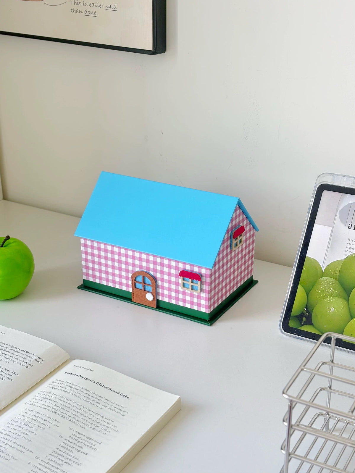 Pink gingham house shaped tissue box cover angled beside an open book
