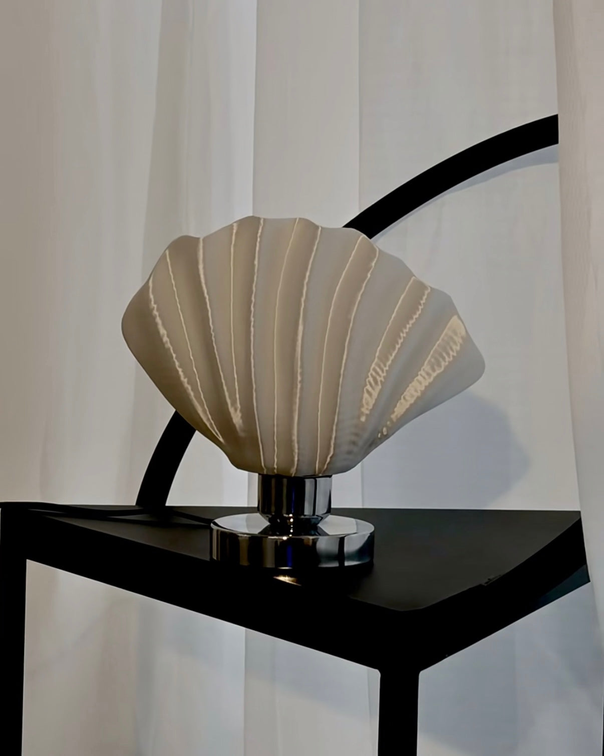 Decorative shell lamp on a black stand with a white curtain background