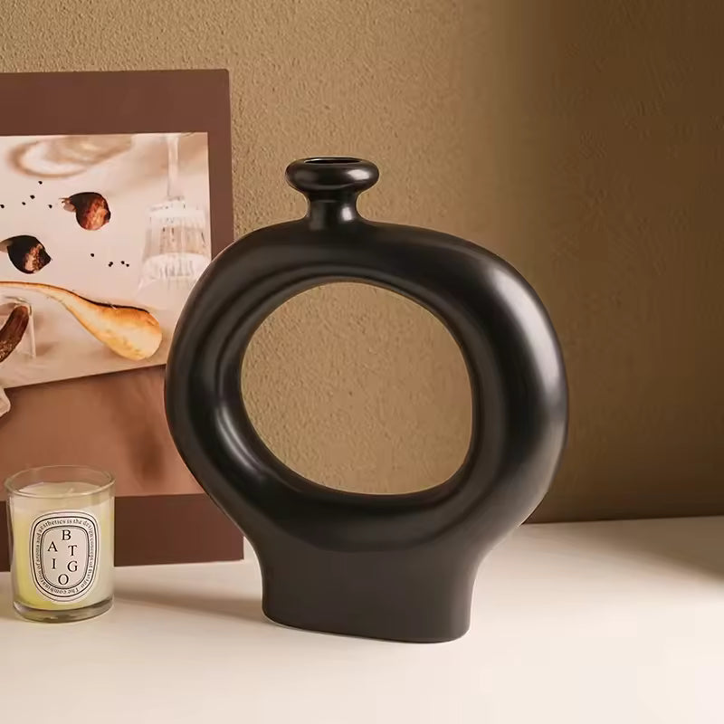 Black ceramic vase with circular design on a beige surface next to a framed picture and candle.