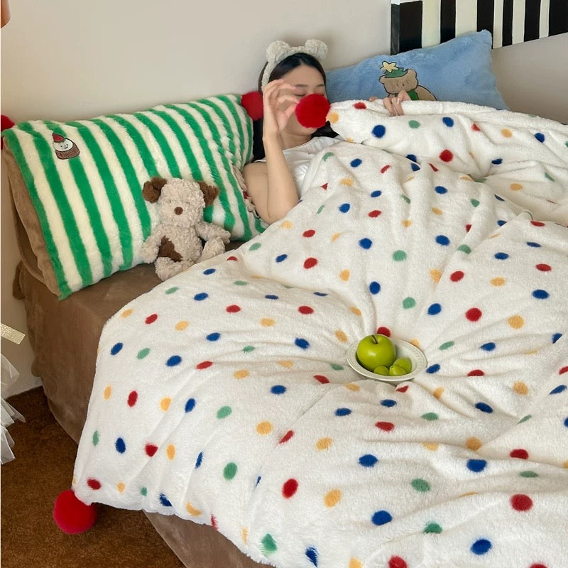 Person lying in bed under a polka dot blanket with colorful pillows and a teddy bear.