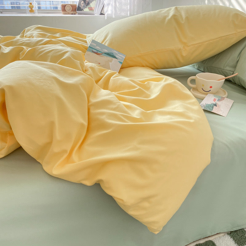 Yellow blanket on a bed with a smiley face mug and book in the background