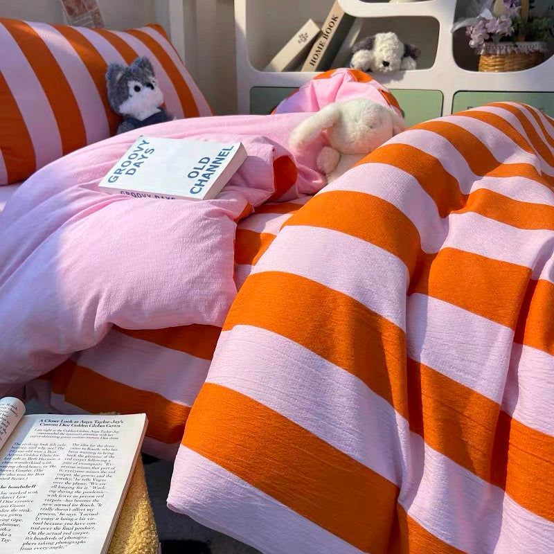 A cozy bed setup featuring a pink and orange striped duvet cover and matching pillowcase, styled with plush toys and an open book in a bright room.